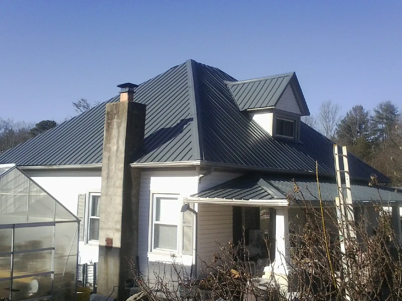 Dark blue standing seam metal roof on a white farmhouse with dormer — Slate & Tile Roof Repair by Roofing Brothers in Prineville