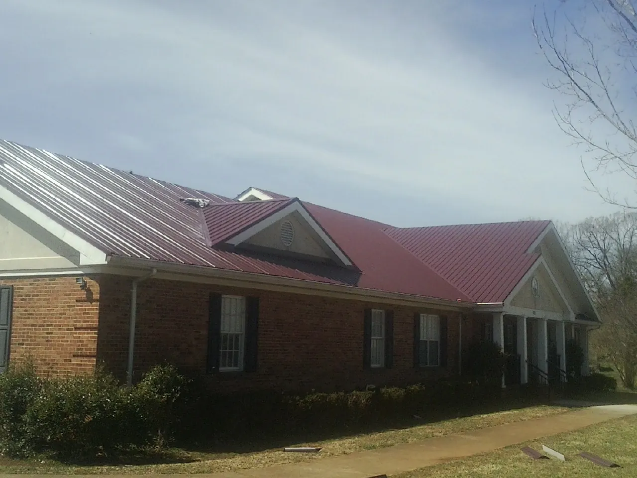 Red metal roof with gabled entries on a long brick building, from a Hail Damage Roof Repair job in Prineville