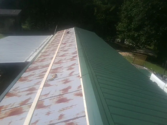 Old rusted panels beside newly installed green metal roofing — Wind Damage Roof Repair by Roofing Brothers in Prineville