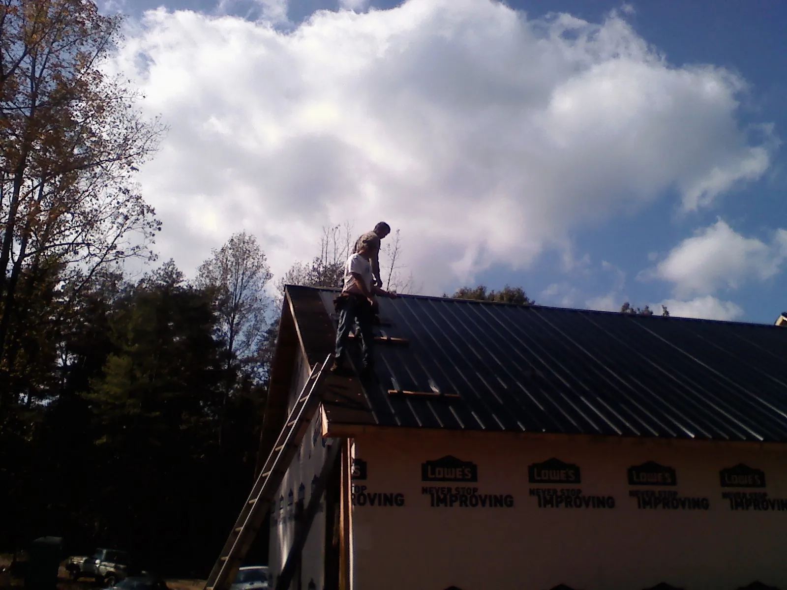 Roofer fastening dark metal panels high against a cloudy sky, from a Roof Inspection job in Prineville