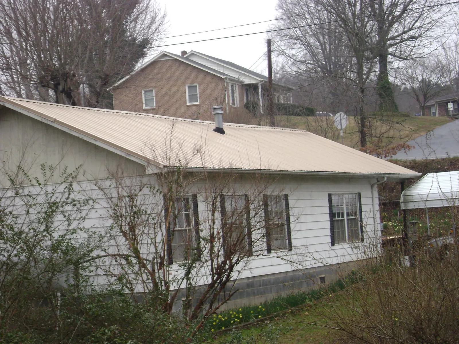 Tan metal roof on a white sided house set into a hillside — Commercial Roofing by Roofing Brothers in Prineville